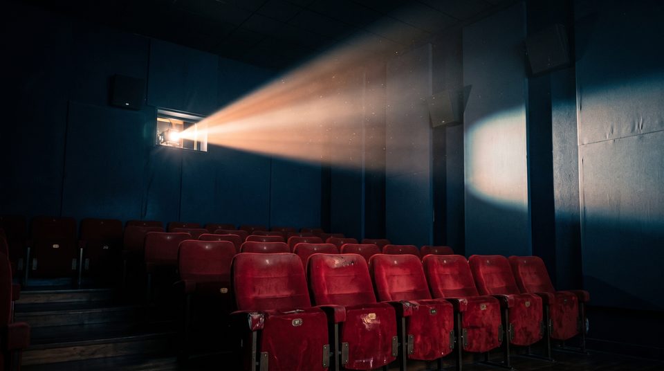 Petite salle de cinéma vide, vue du fond, traversée par le faisceau poussiéreux du projecteur